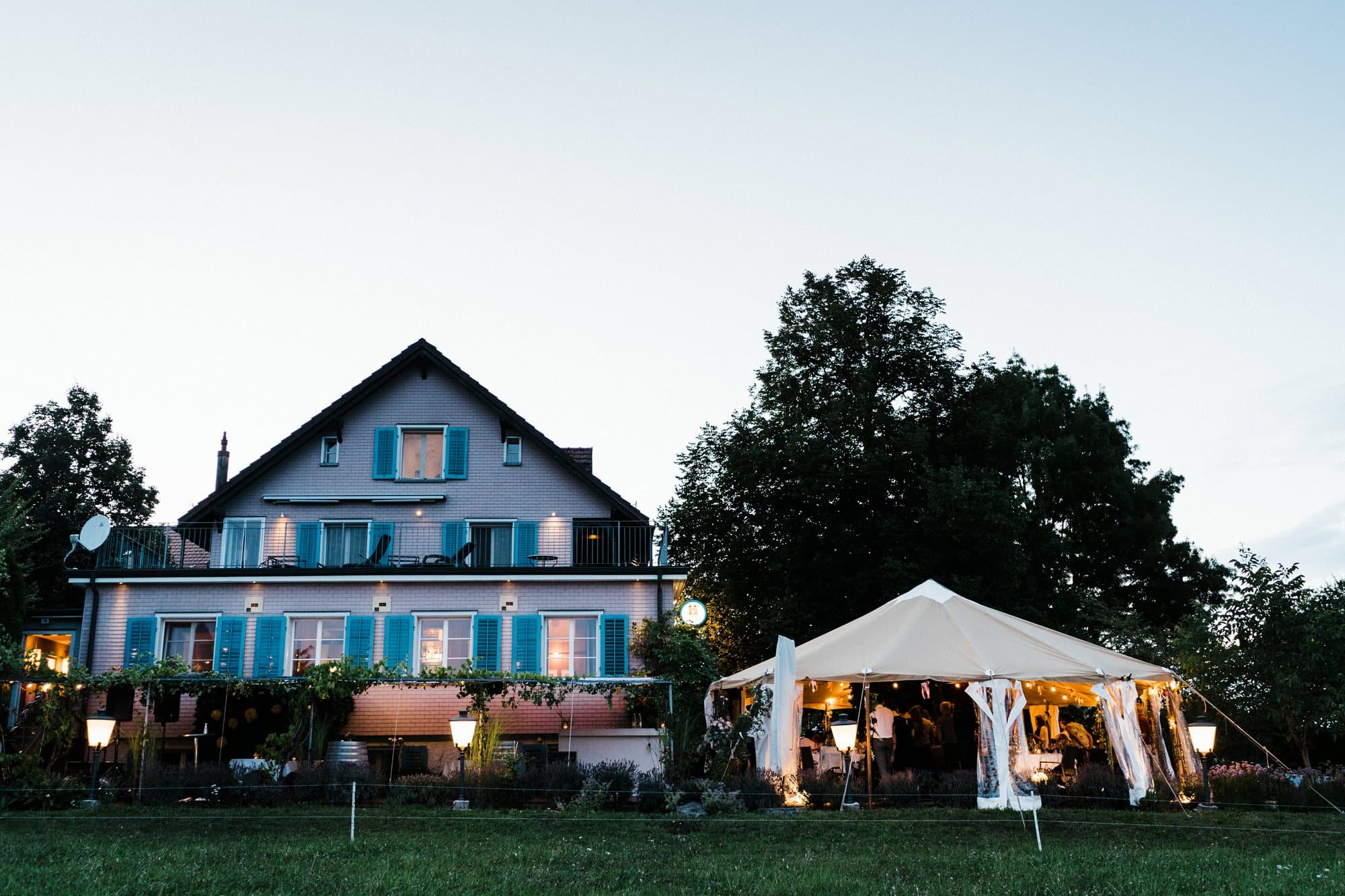 Lit tent beside a farmhouse at a wedding in the evening