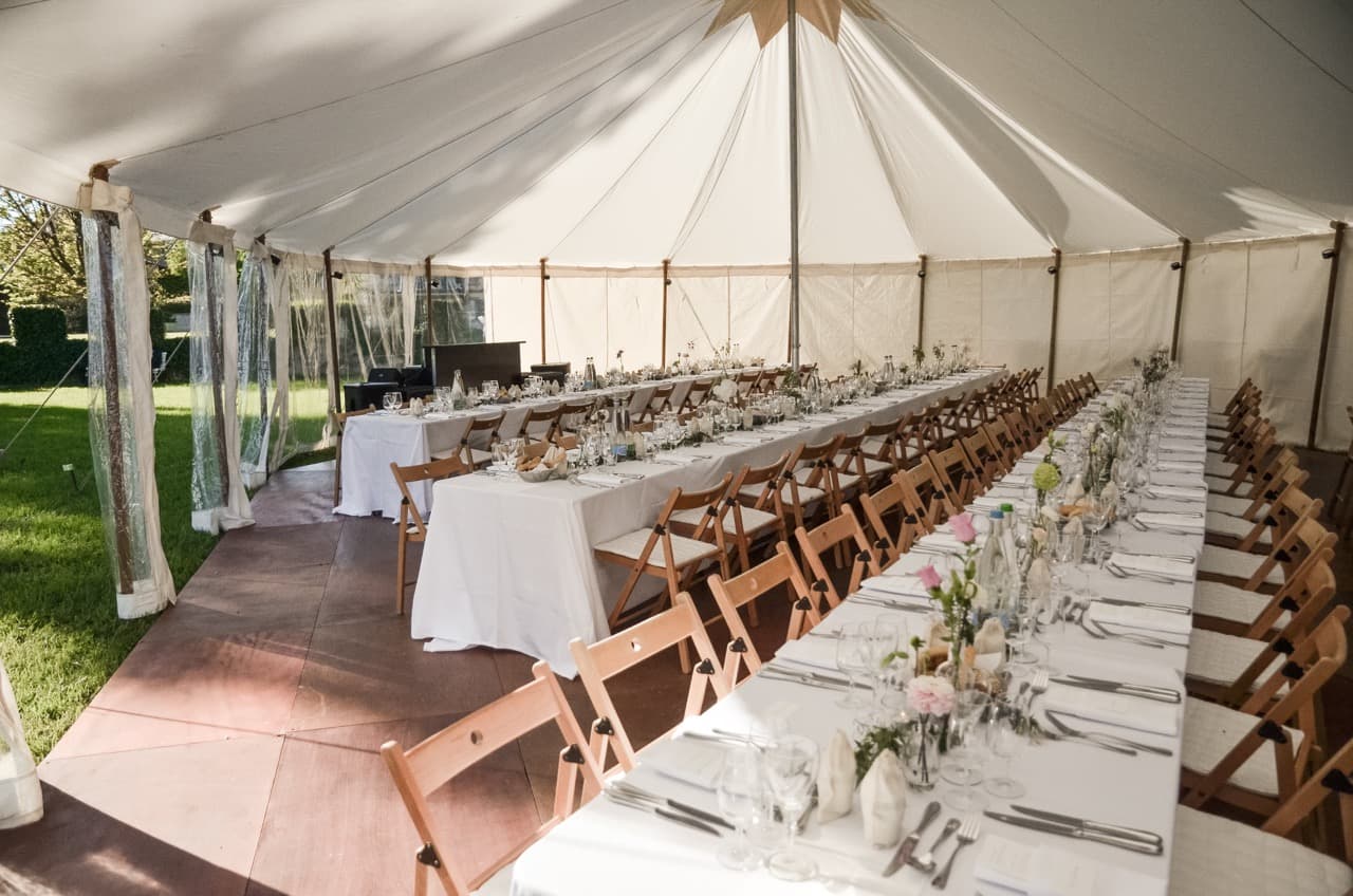Laid wedding table with wooden chairs under a white fabric tent