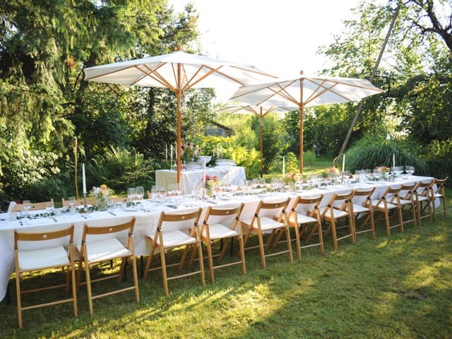 Long laid table with wooden chairs and parasols in a garden