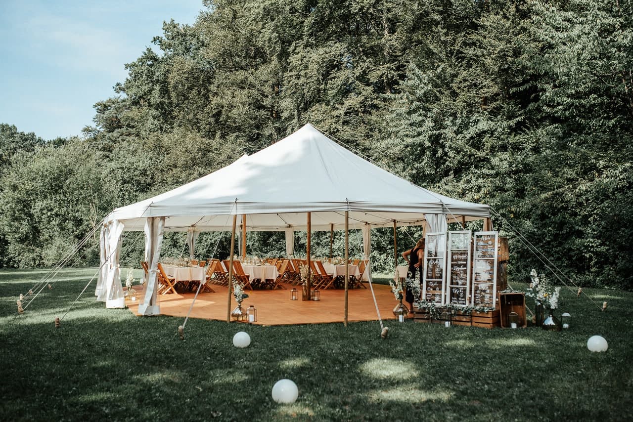 White fabric tent with wooden poles on a garden lawn